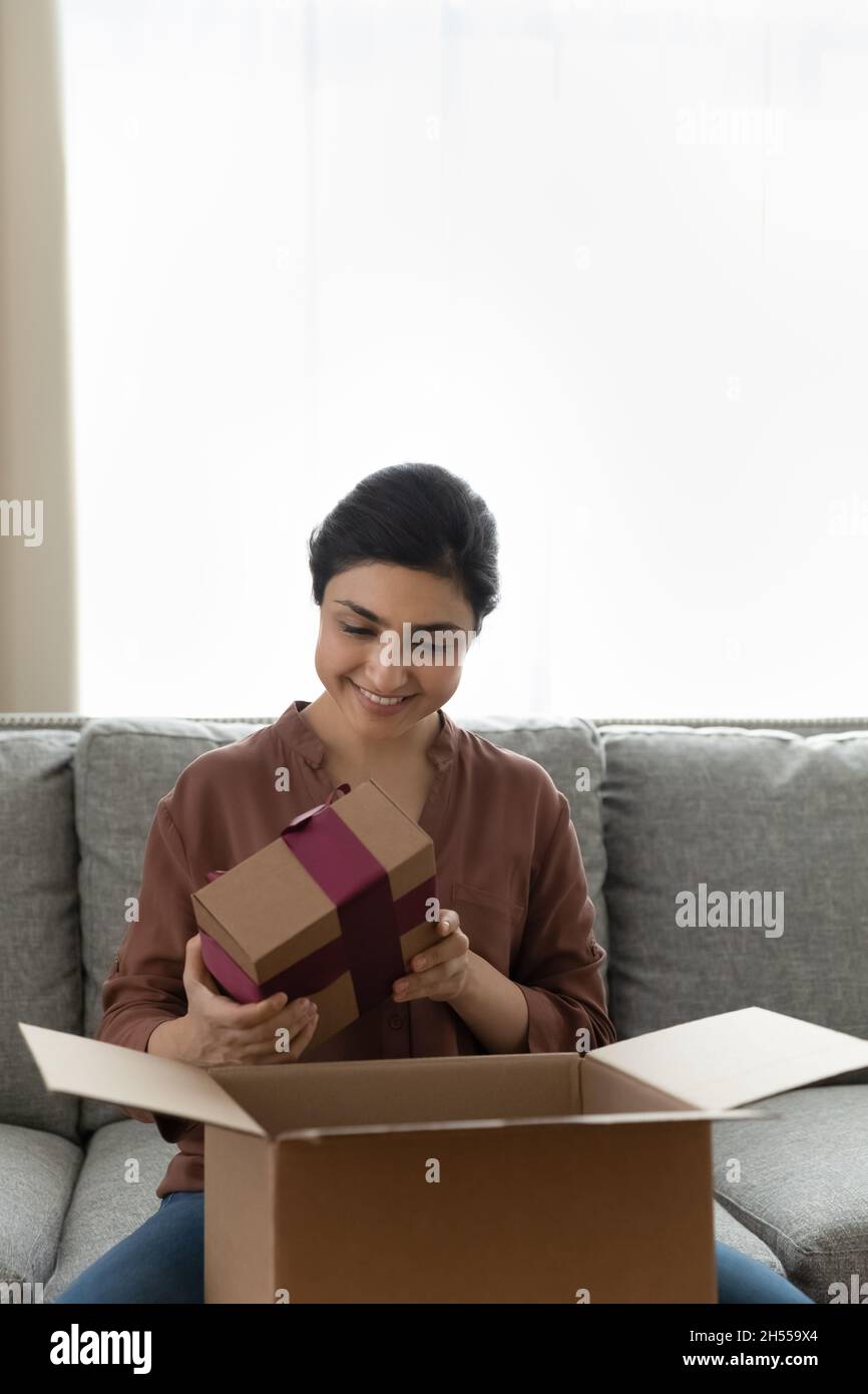 Glückliche indische Frau hält Geschenkbox, während sie das Paket auspackt Stockfoto