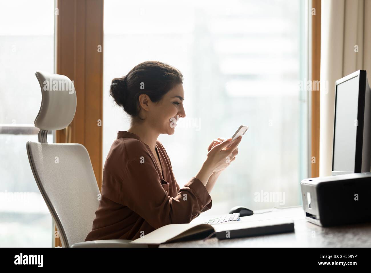Lächelnde indische Mitarbeiter ruhen sich am Arbeitsplatz mit dem Smartphone aus Stockfoto