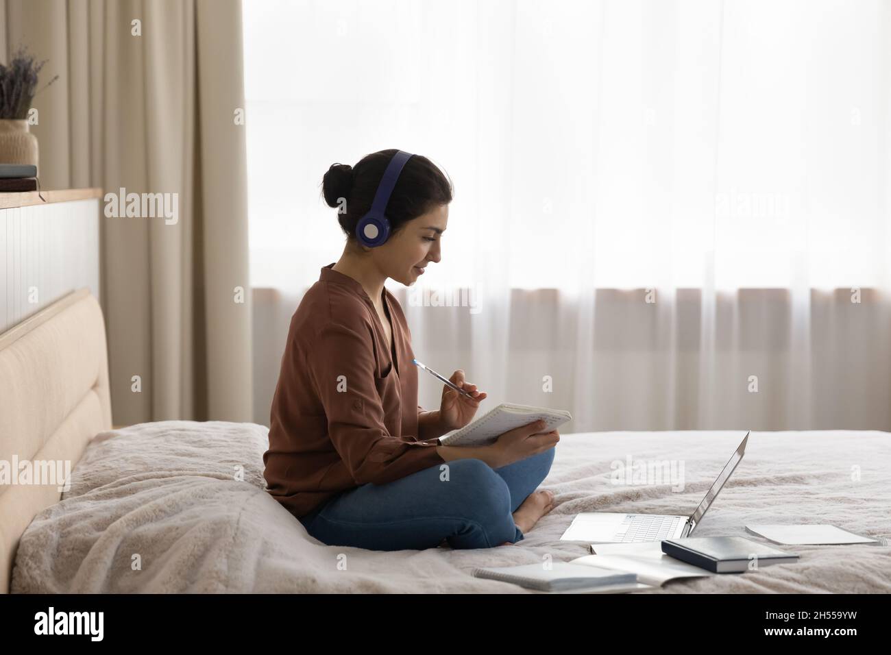 Indische Frau sitzt auf dem Bett hören Audio-Kurs aus der Ferne studieren Stockfoto