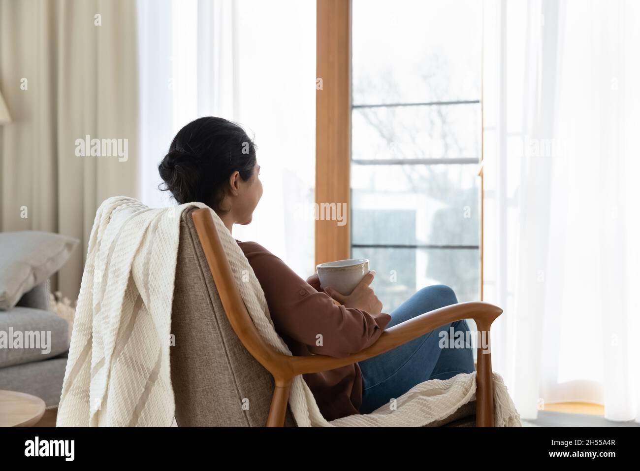 Ruhige indische Frau entspannen Sie sich auf einem bequemen Sessel mit Teetasse Stockfoto