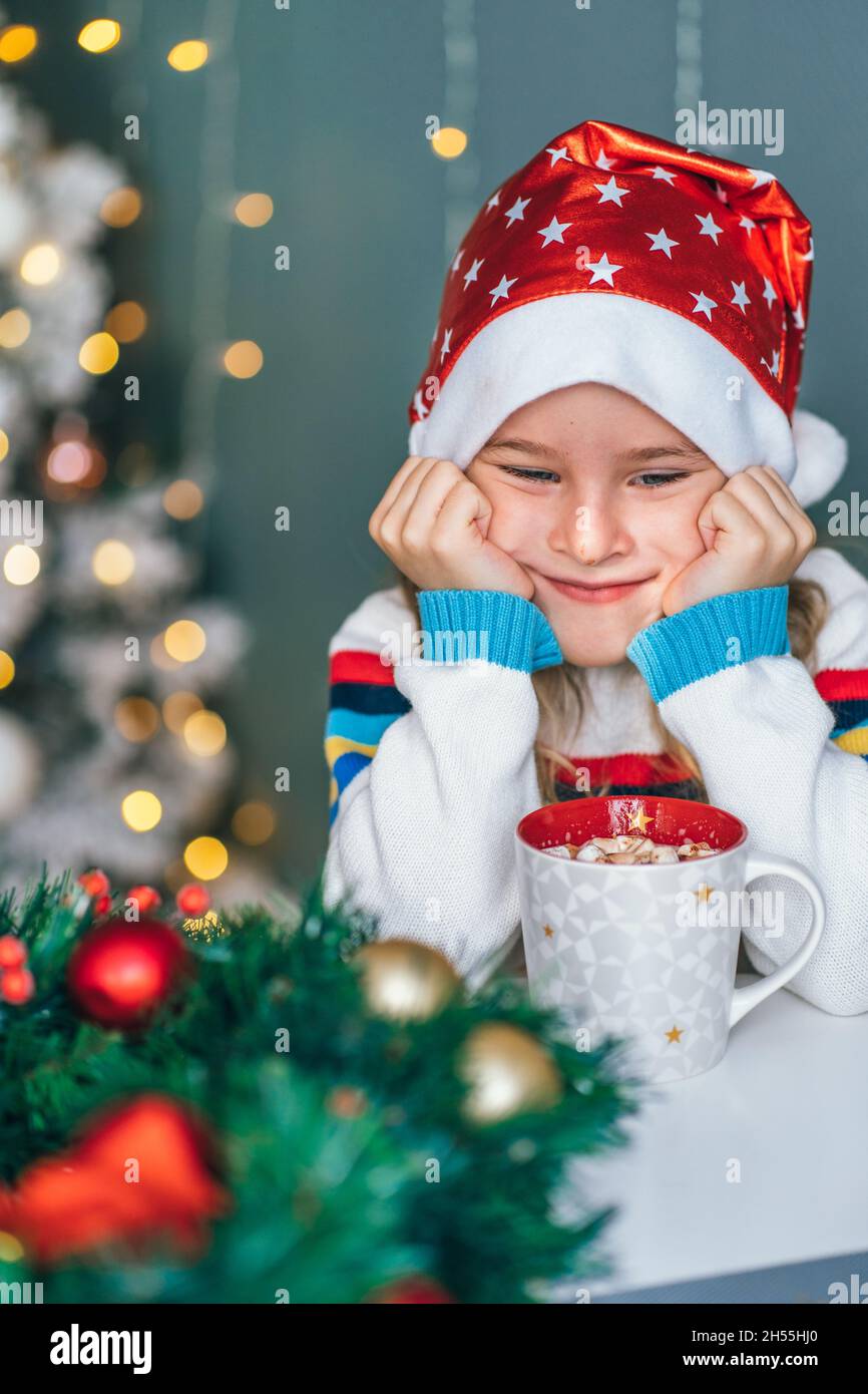 Santa kleiner Helfer mit dekorativem weihnachtsbaum im Hintergrund. Kleines Mädchen verärgert und enttäuscht. Stockfoto