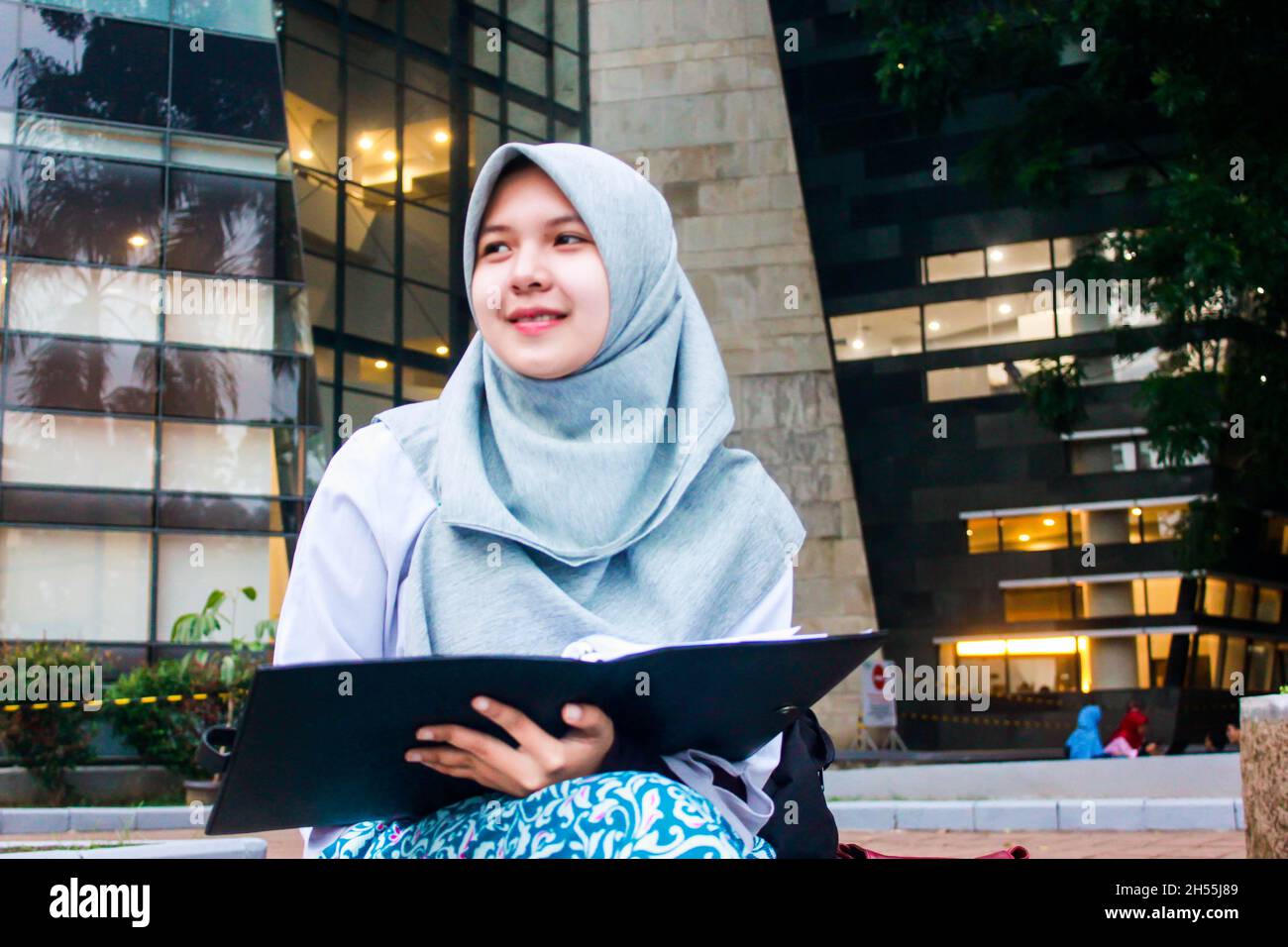 Südostasiatische muslimische College-Frau mit himmelblau gefärbten Hijab hält ein Buch. Stockfoto