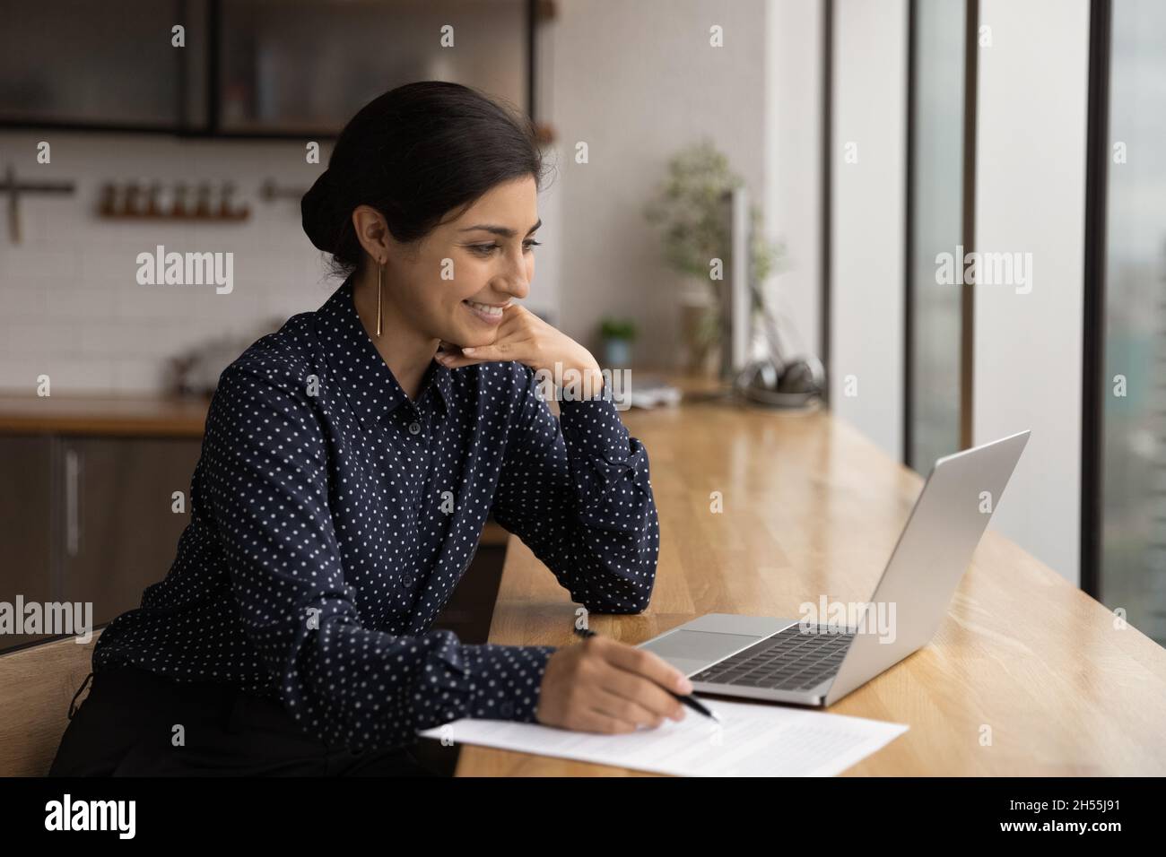 Glückliche junge indische Frau, die Notizen auf dem Laptop-Bildschirm schreibt. Stockfoto