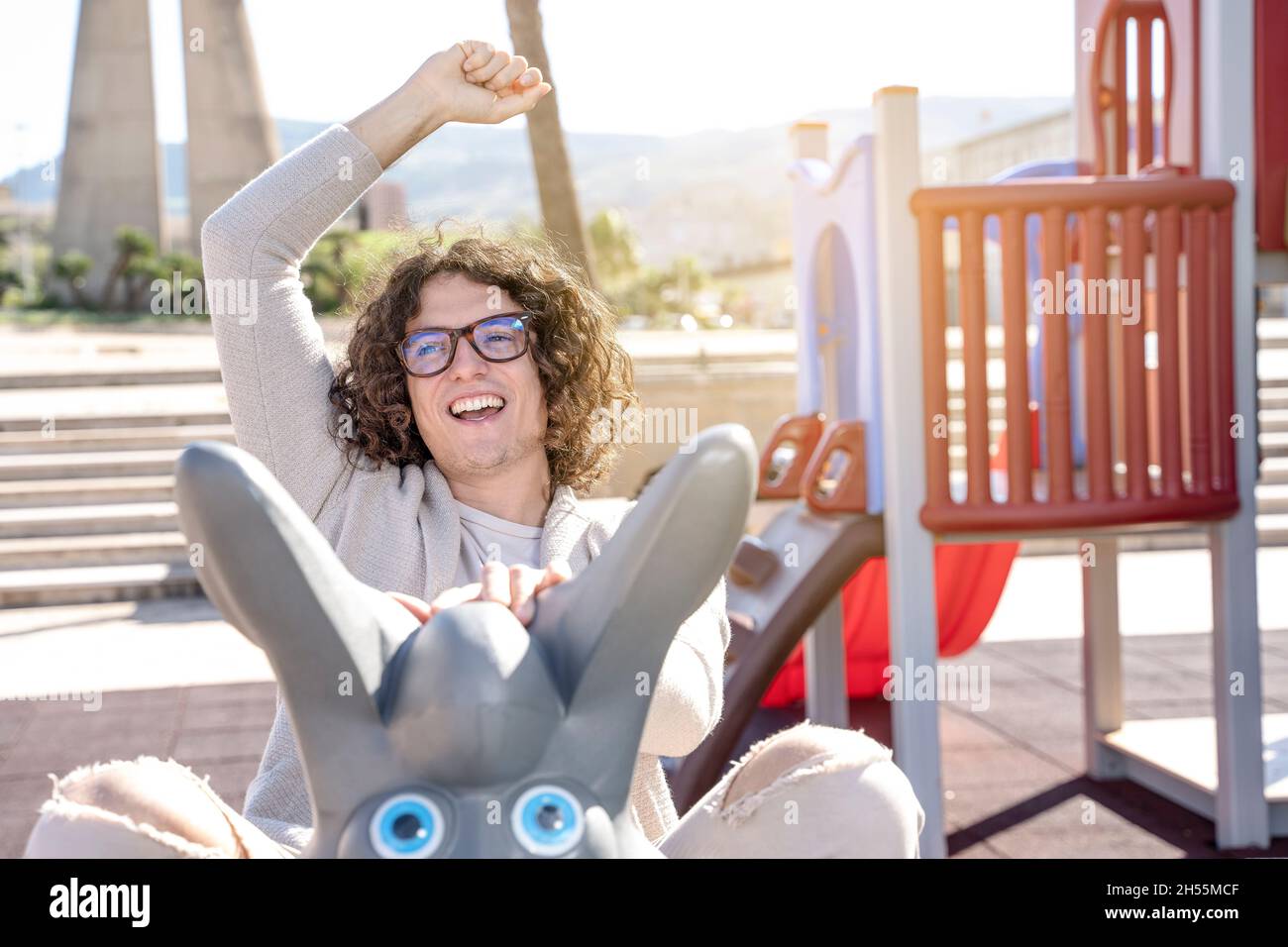 Junger, fröhlich lächelnder Mann schaukelt auf dem Spielplatz Stockfoto