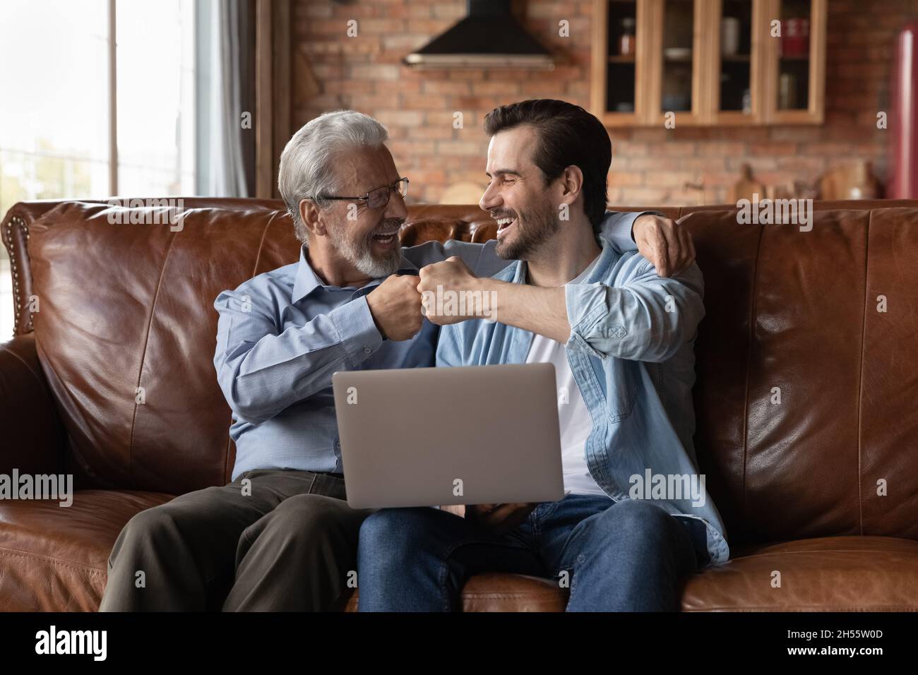Männer verschiedener Altersgruppen sitzen auf dem Sofa und halten Laptop-Fäuste fest Stockfoto