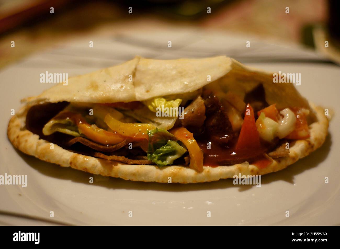 Nahaufnahme von Döner Kebab und Salat mit heißer Sauce auf einem Teller mit defokussiertem Tischplattenhintergrund Stockfoto