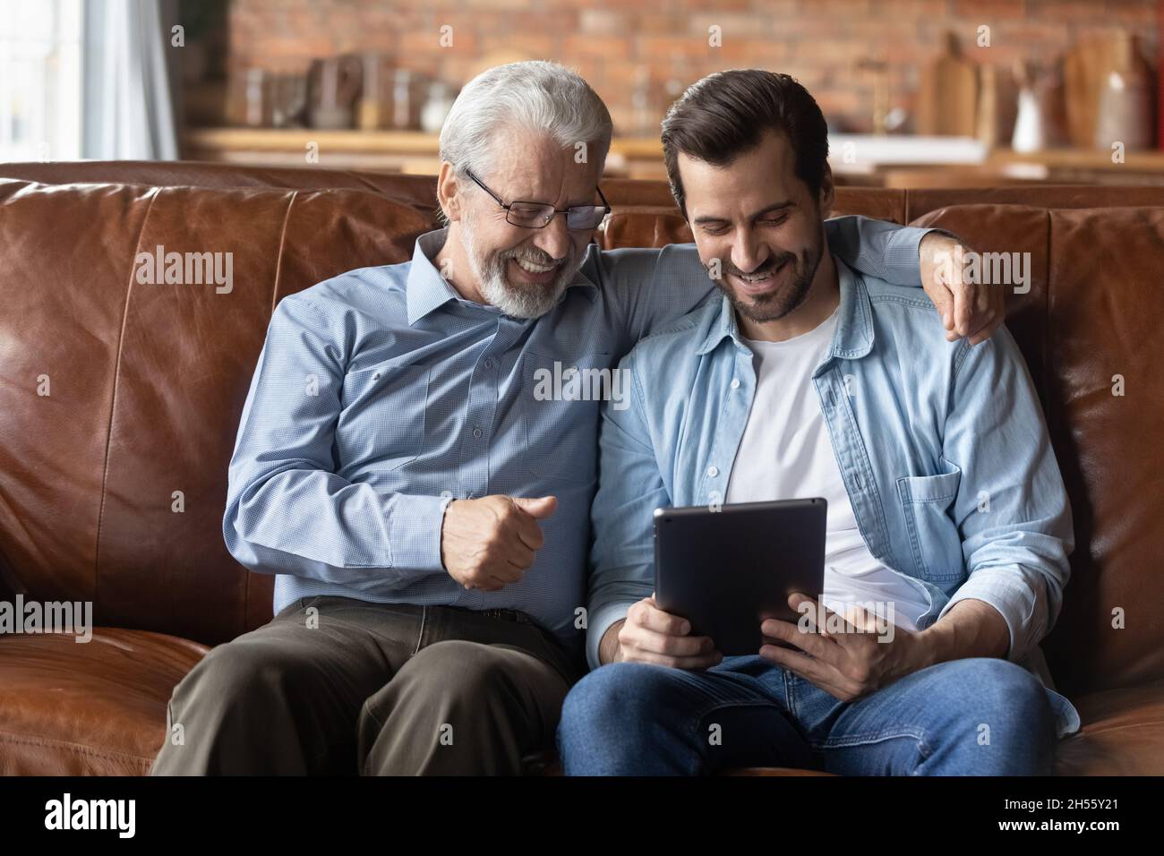 Ältere Männer mit Brille verwenden einen Tablet-Computer mit einem erwachsenen Sohn Stockfoto