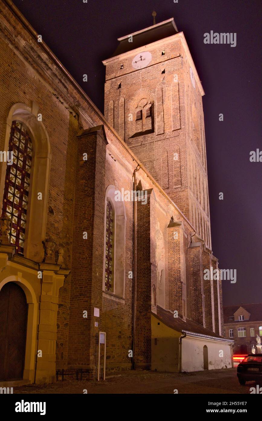 Altes Kirchengebäude bei Nacht in der Stadt Zagan in Polen. Die roten Backsteinwände der Kirche werden von elektrischen Lampen beleuchtet. Stockfoto