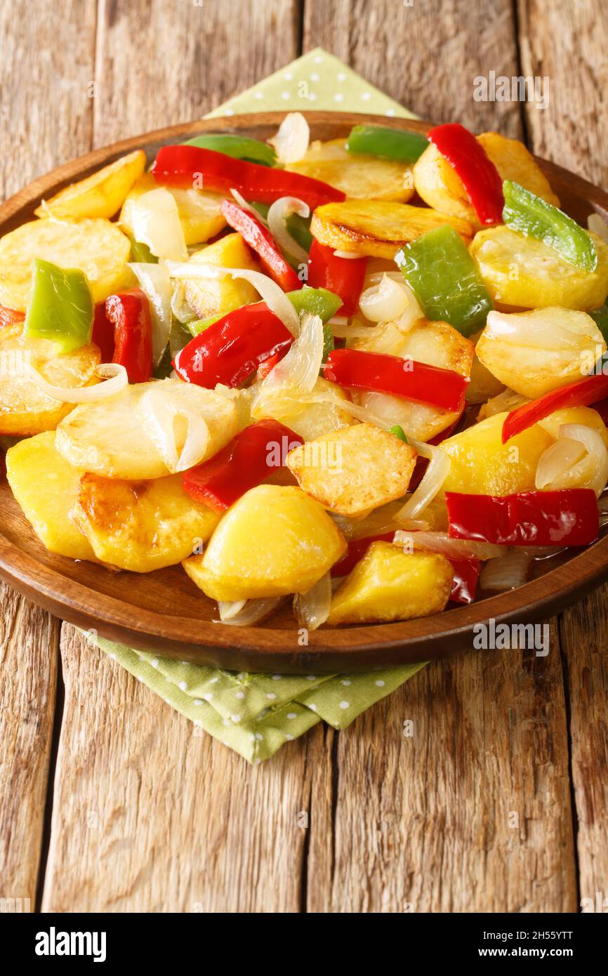 Gebratene Kartoffeln mit Zwiebeln und roten und grünen Paprika Nahaufnahme in einem Teller auf dem Tisch. Vertikal Stockfoto