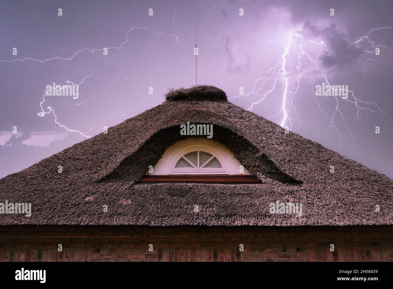 Gewitterhimmel mit Blitz und Donner über einem Strohdach mit Blitzableiter. Konzept für Brandrisiko- und Sachversicherung. Stockfoto