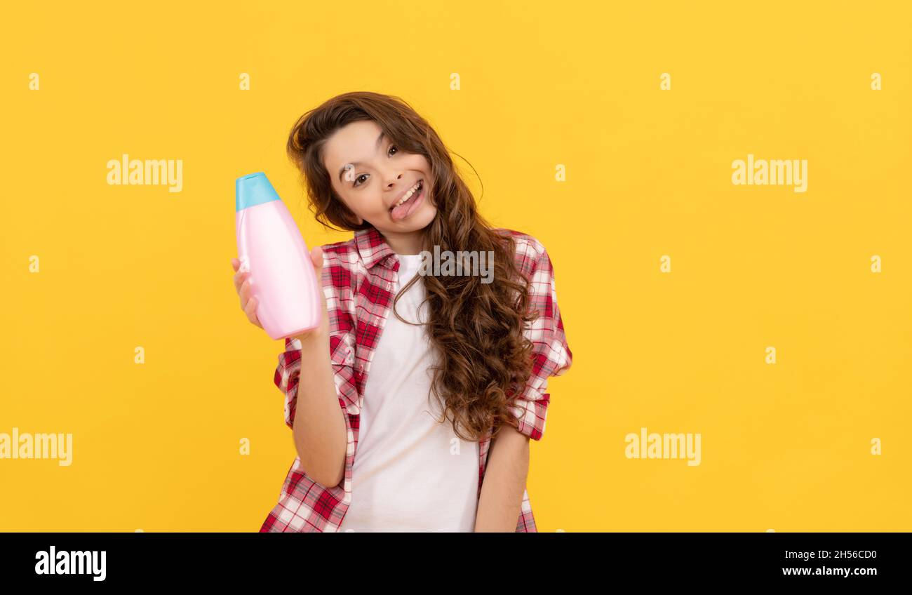 Happy teen Mädchen mit langen lockigen Haaren halten Shampoo-Flasche, präsentiert Produkt Stockfoto