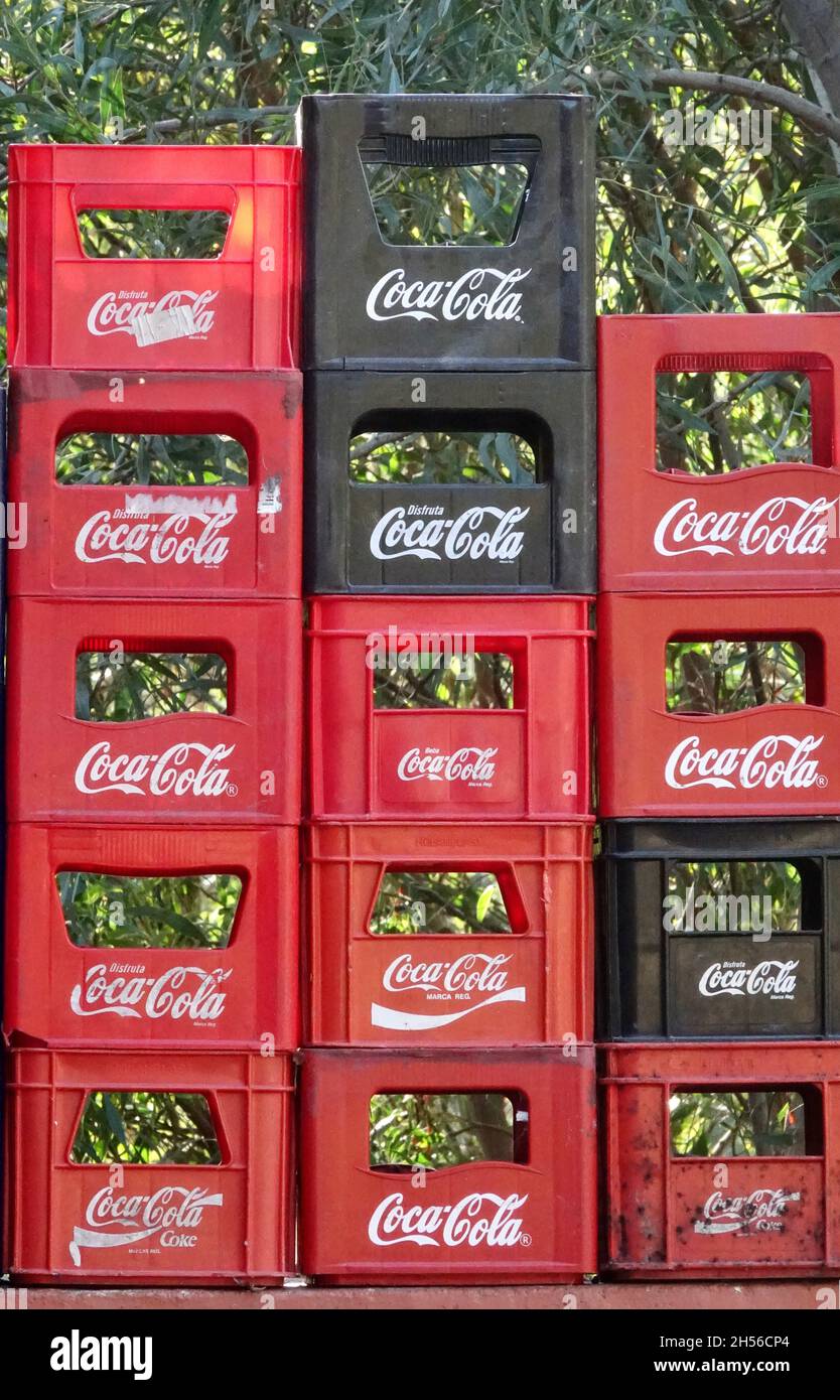 Almuñécar, Spanien; 28. Oktober 2021: Rote und schwarze Coca-Cola-Boxen, die sich draußen neben Bouganvillablumen stapeln Stockfoto