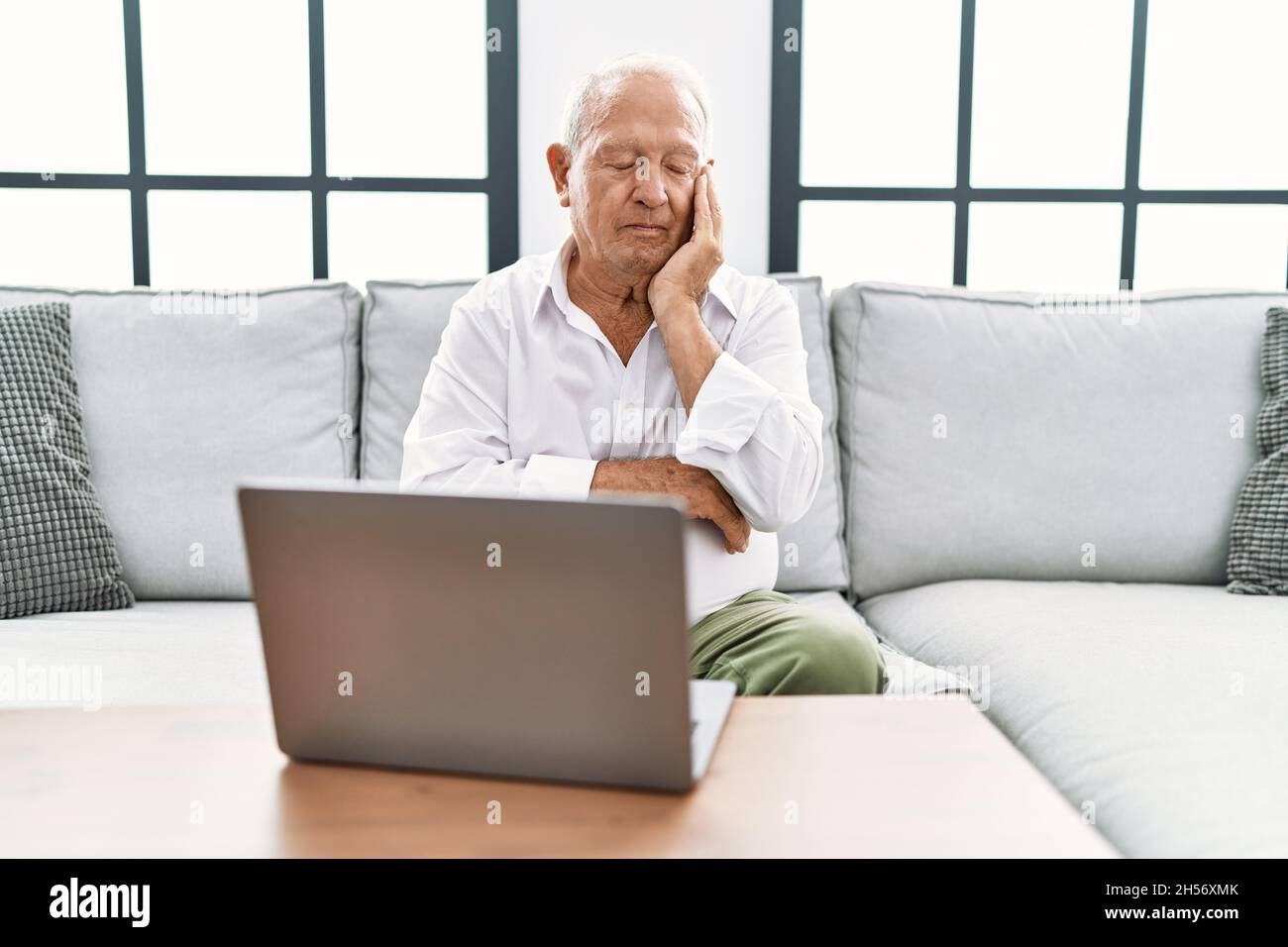Ein älterer Mann, der zu Hause einen Laptop benutzt, sitzt auf dem Sofa