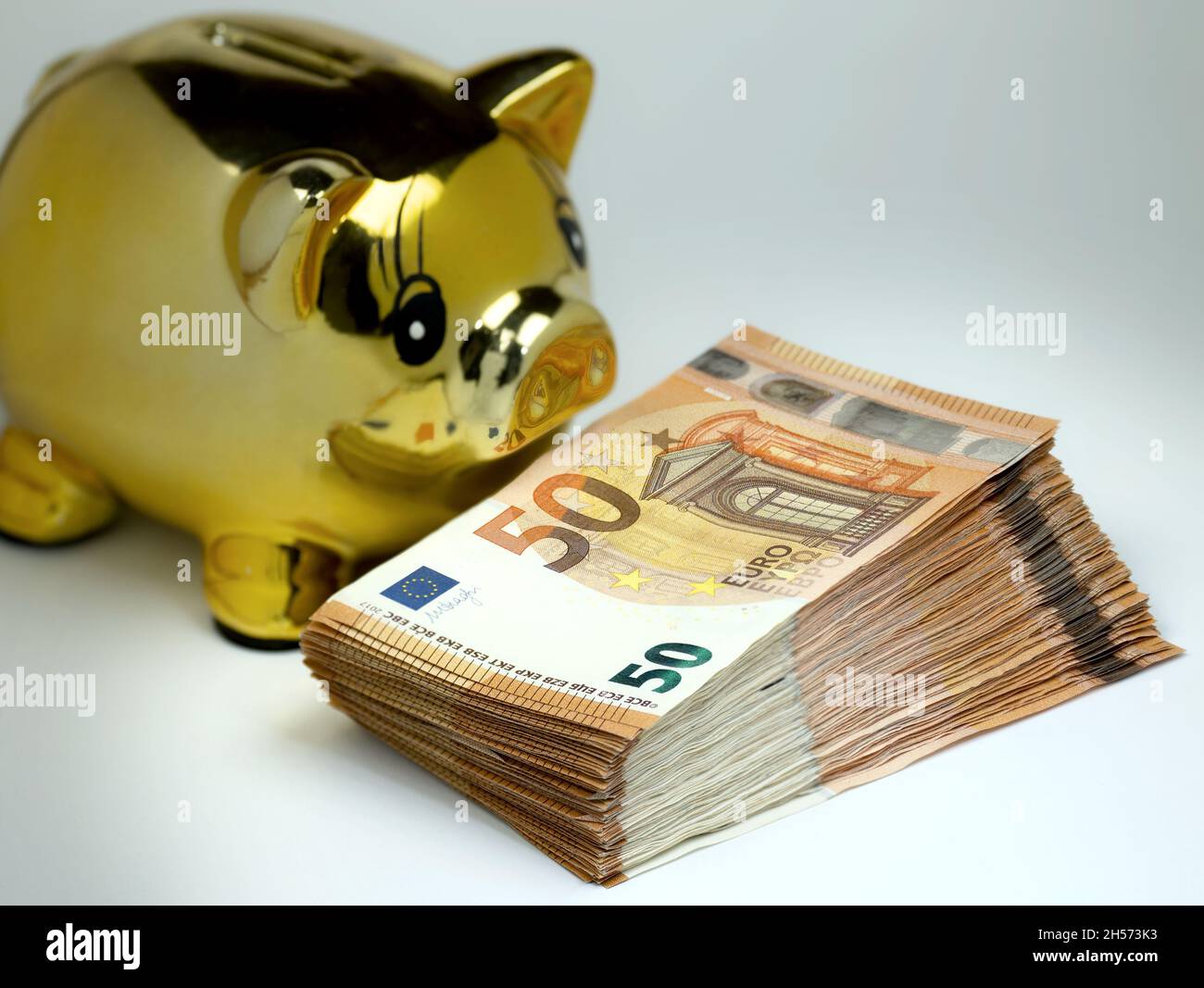 Goldenes Sparschwein mit einem Stapel von 50-Euro-Banknoten im Vordergrund. Stockfoto