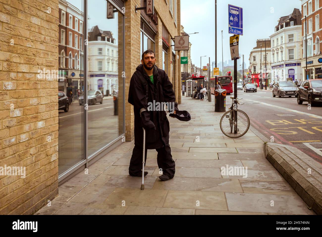 Ein behinderter Mann in der Dalston High Street, der seine Mütze ausstreut und um Geld bittet. Stockfoto