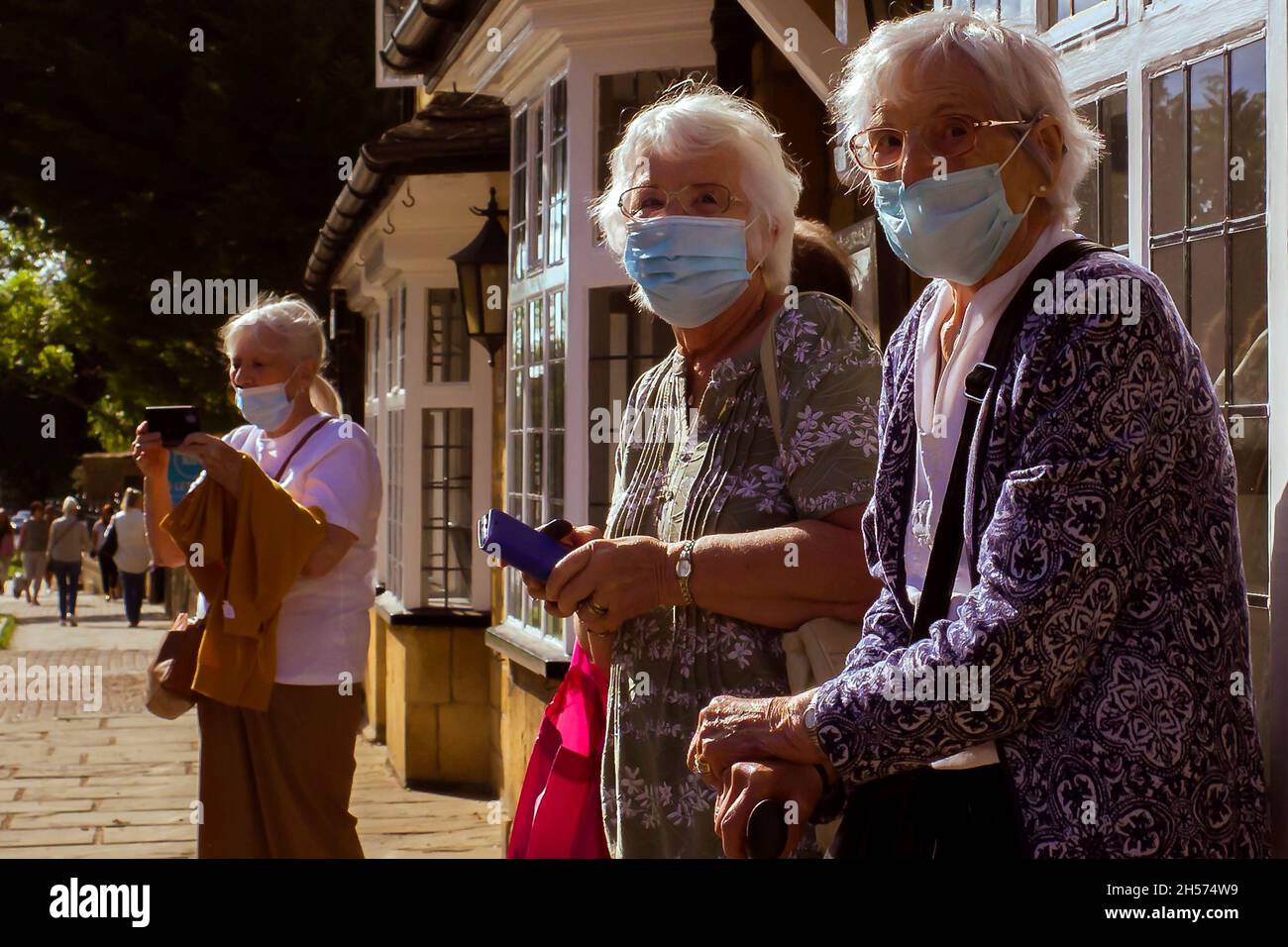 Eine kleine Gruppe älterer Touristen besucht den Broadway in den Cotswolds. Sie tragen Gesichtsmasken als zusätzlichen Schutz vor dem Covid 19-Virus. Stockfoto
