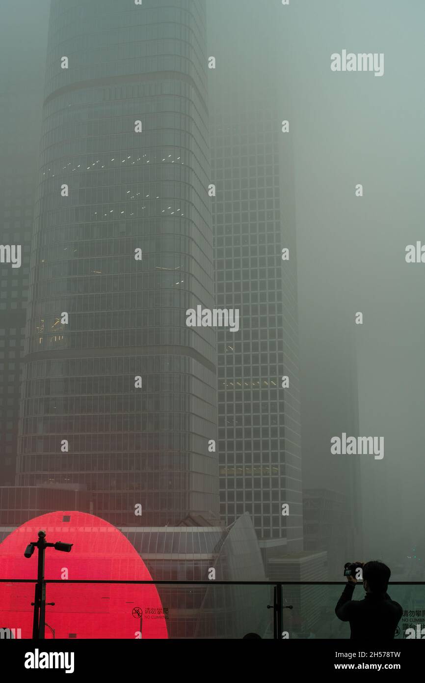 Ein junger Mann fotografiert einen Wolkenkratzer, der in starkem Smog gehüllt ist, im Geschäftszentrum von Peking, China. 06-Nov-2021 Stockfoto