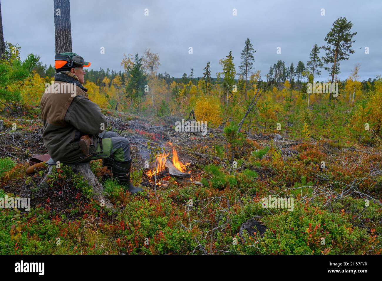 Hunter sitzt auf einem Stumpf vor einem Feuer auf der Suche nach Elchen, Bild aus vasternorrland schweden. Stockfoto
