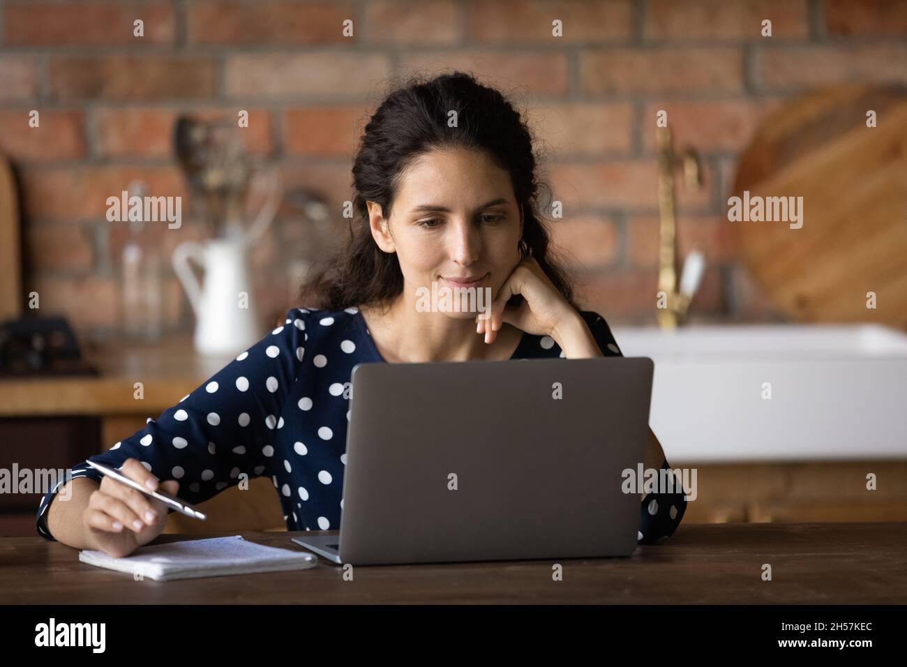 Nachdenkliche lateinische Frau sehen sich das Webinar auf einem Laptop in der Küche zu Hause an Stockfoto
