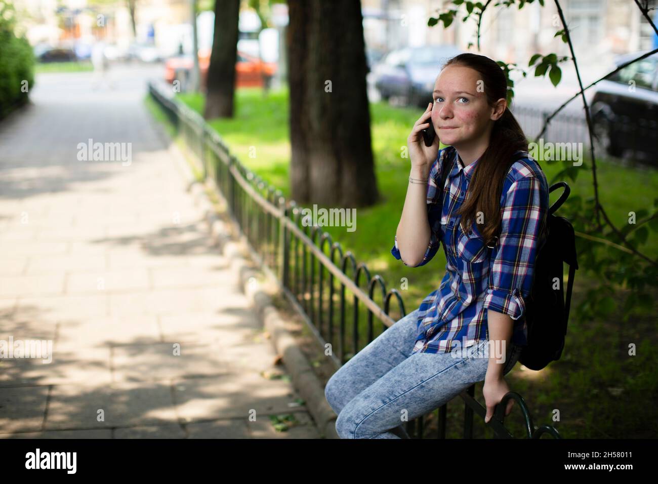 Ein Mädchen spricht auf ihrem Handy, während es auf dem Platz sitzt. Stockfoto