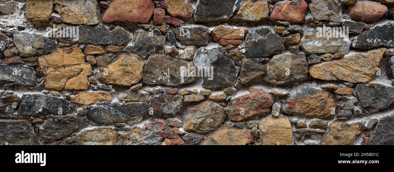 Alte raue Wand aus vielfarbigem Naturstein. Verlassene Gebäudetextur Stockfoto