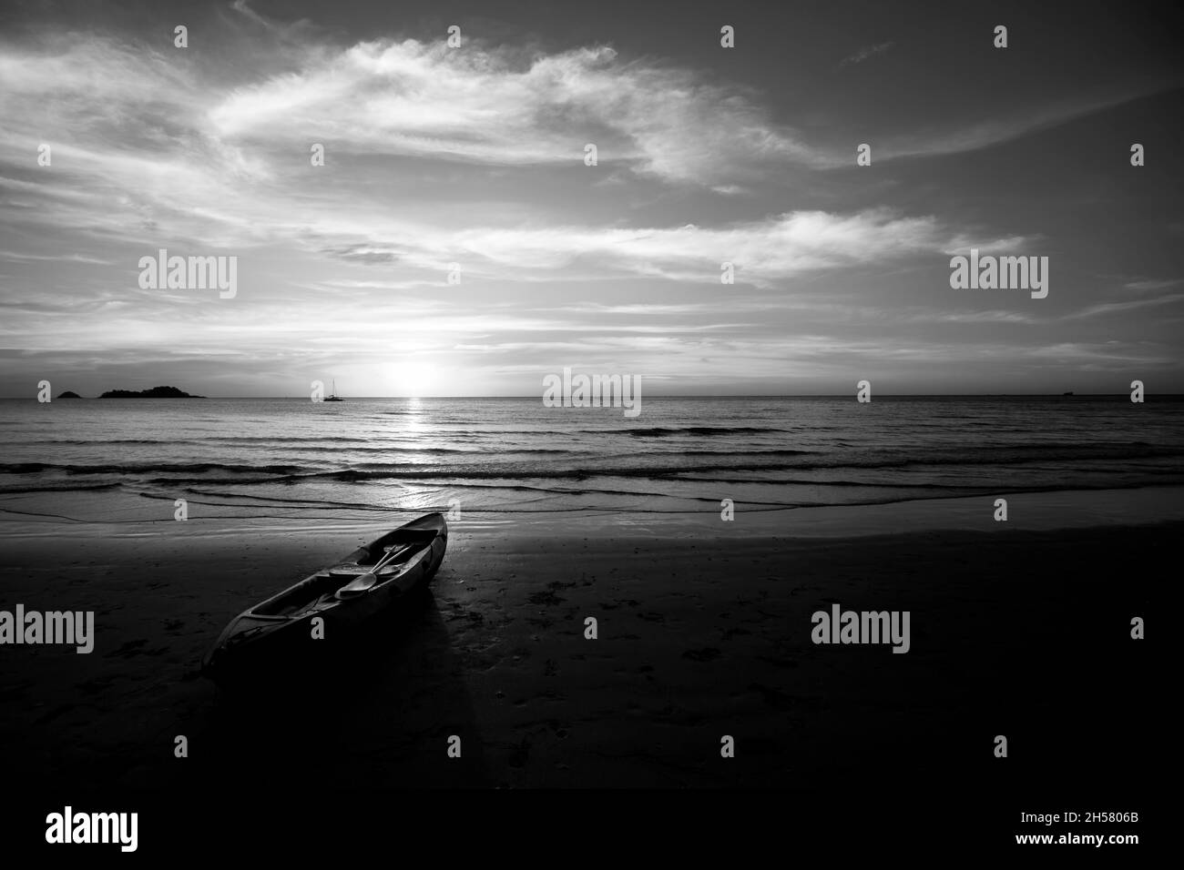 Ein Kajak liegt während eines Sonnenuntergangs am tropischen Strand. Schwarzweiß-Foto. Stockfoto
