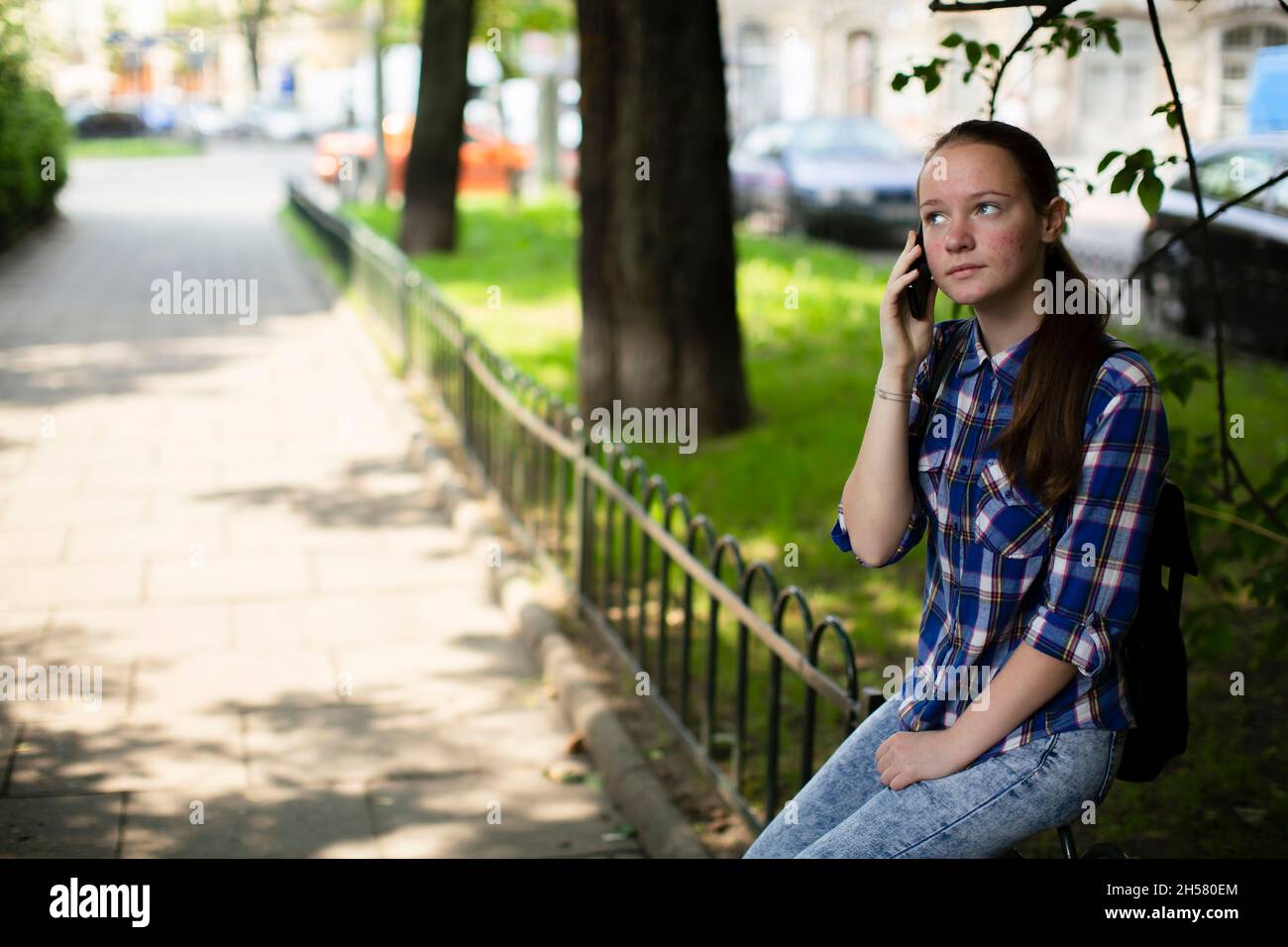 Ein Teenager-Mädchen spricht auf ihrem Handy, während es auf dem Platz sitzt. Stockfoto