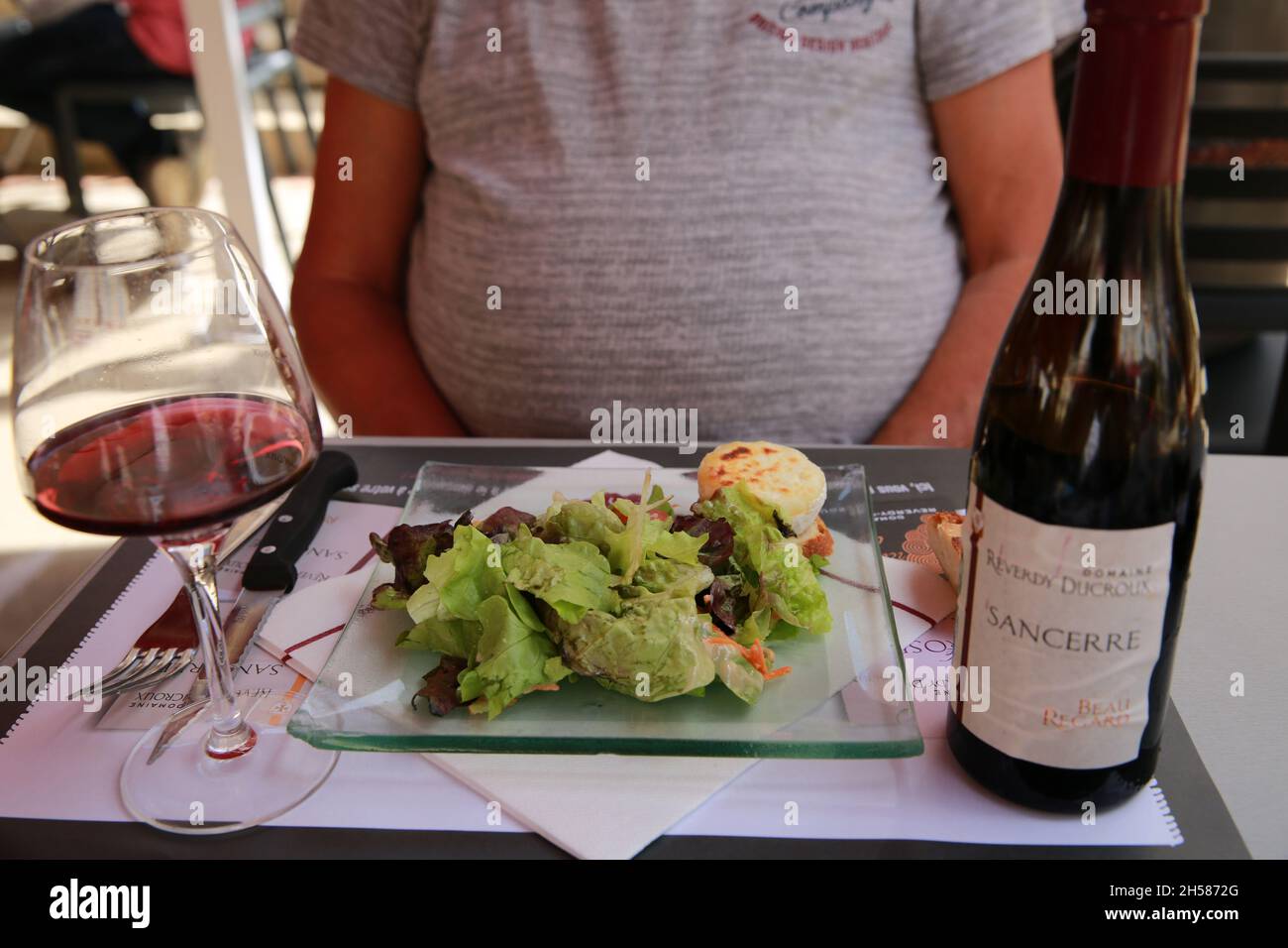 Mittelteil eines Mannes mit einem großen Magen, der eine Mahlzeit mit einem Verkauf und Rotwein genießt. Stockfoto