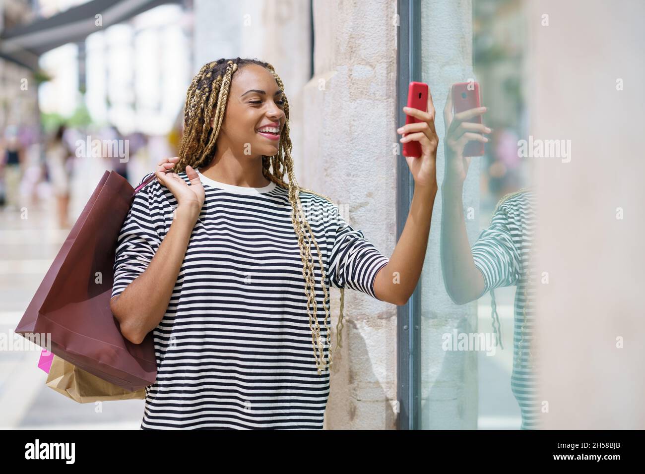 Die junge schwarze Frau fotografiert mit ihrem Smartphone ein Schaufenster in einer Einkaufsstraße. Stockfoto