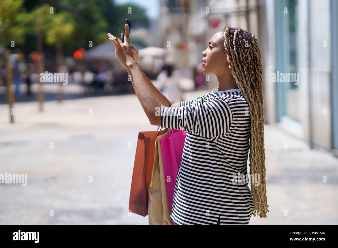 Schwarzes Mädchen fotografiert etwas in einer Einkaufsstraße mit ihrem Smartphone. Stockfoto
