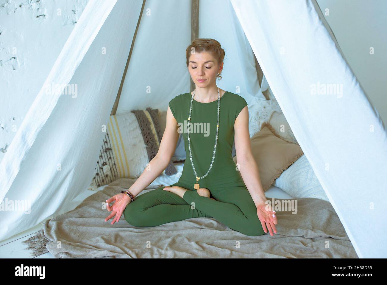Schönes und schlankes Mädchen in grüner Sportkleidung, meditiert oder macht Yoga zu Hause Stockfoto