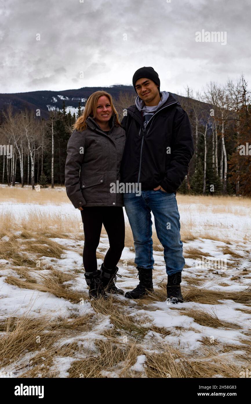 Paar posiert vor der Baumgrenze an dunklen bewölkten Tag im Winter. Kleine Menge Schnee, totes Gras. Berg im Hintergrund Stockfoto