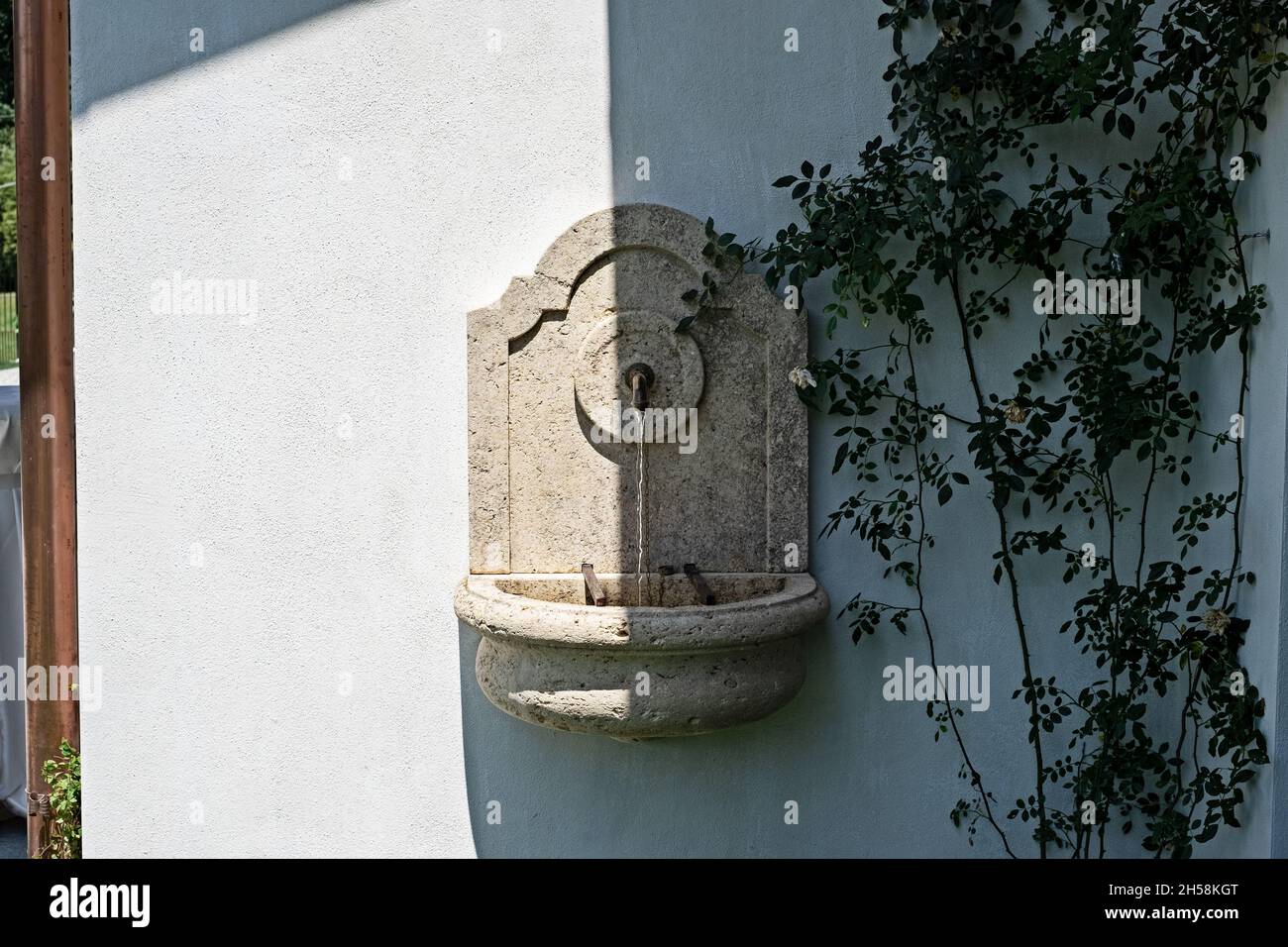 Kleiner Brunnen mit fließendem Wasser, halb im Schatten, an der Seite eines Hauses in Norditalien Stockfoto