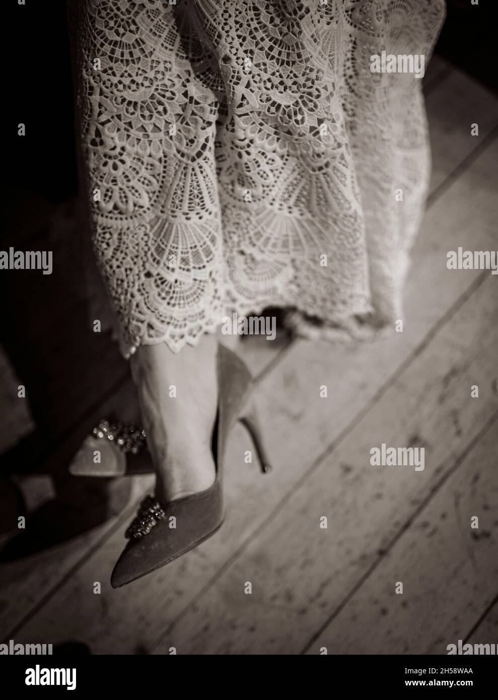 Eine Frau, die sich mit gekreuzten Füßen hingesetzt hat, trägt ein Spitzenkleid und stilvolle Schuhe Stockfoto
