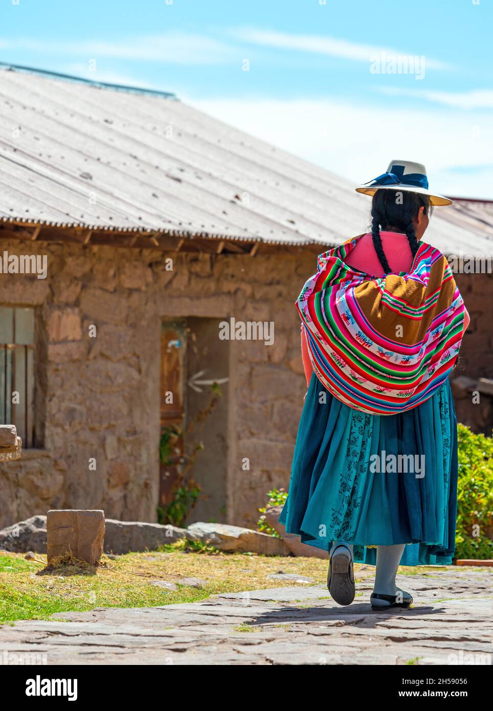 Indigene peruanische Quechua-Frau in traditioneller Kleidung, die in einer Straße auf der Insel Taquile am Titicaca-See in Peru spazierengeht. Stockfoto