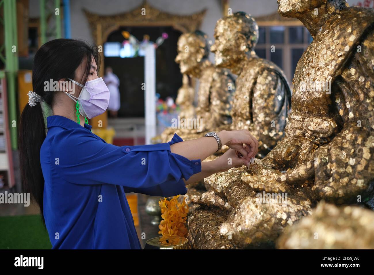 Eine asiatische Frau vergoldet ein dünnes Blattgold auf einer buddha-Statue in einem thailändischen Tempel in Thailand. Befestigen oder kleben Sie Blattgold auf den Arm der Buddha-Statue. Stockfoto