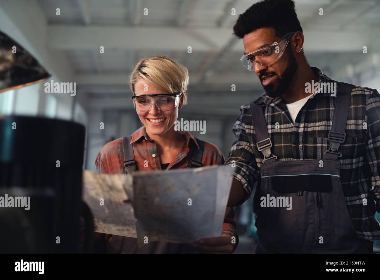 Porträt junger birazialer Industriekollegen, die in Innenräumen in einer Metallwerkstatt arbeiten, lächelnd. Stockfoto