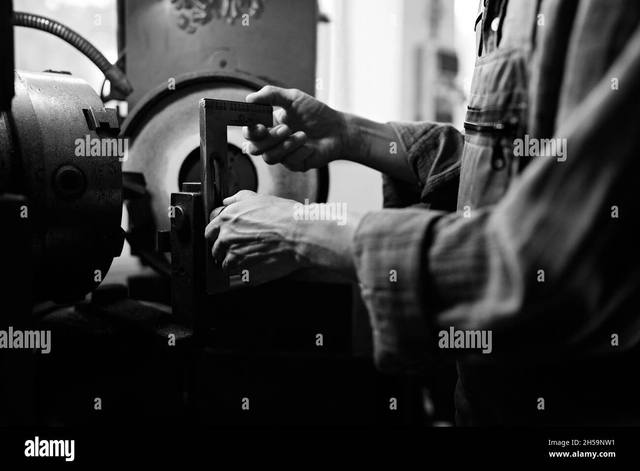 Schwarz-weiße Nahaufnahme der man Hand mit Bremssattel messen Stahlkomponente in Innenräumen in Metallwerkstatt. Stockfoto