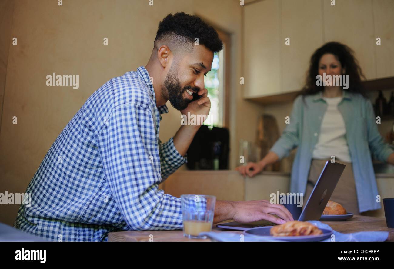 Glückliches Paar mit Laptop, das drinnen im Baumhaus, Wochenendausflug und Remote Office sitzt und sich ausruht. Stockfoto