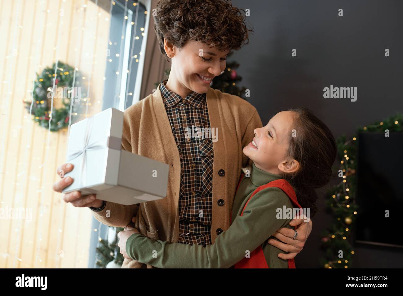 Happy hübsches Mädchen umarmt Mutter mit Geschenkbox, während sie zu Weihnachten gratuliert Stockfoto