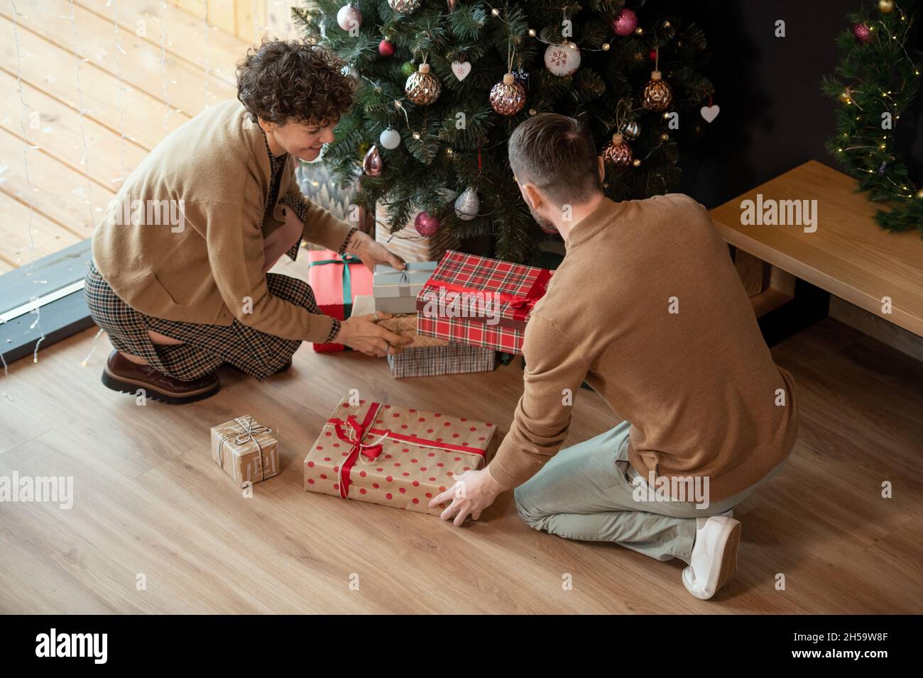 Eltern legen Weihnachtsgeschenke unter geschmückten Baum, während sie es für Kinder vorbereiten Stockfoto