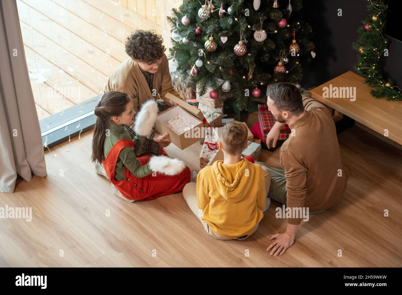Die ganze Familie sitzt um den geschmückten Baum herum und öffnet gemeinsam Weihnachtsgeschenke Stockfoto