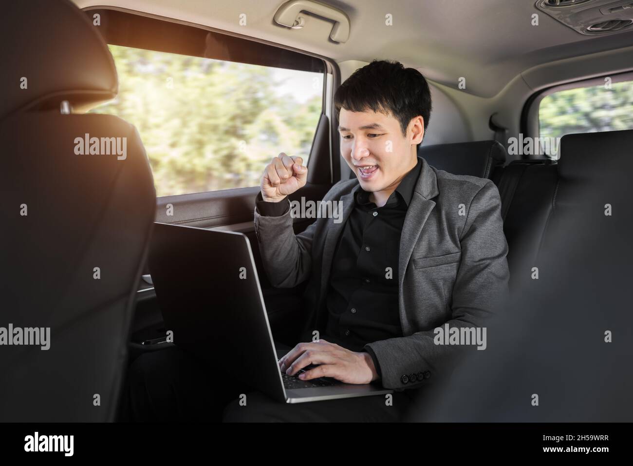 Erfolgreicher junger Geschäftsmann, der auf dem Rücksitz des Autos einen Laptop verwendet Stockfoto