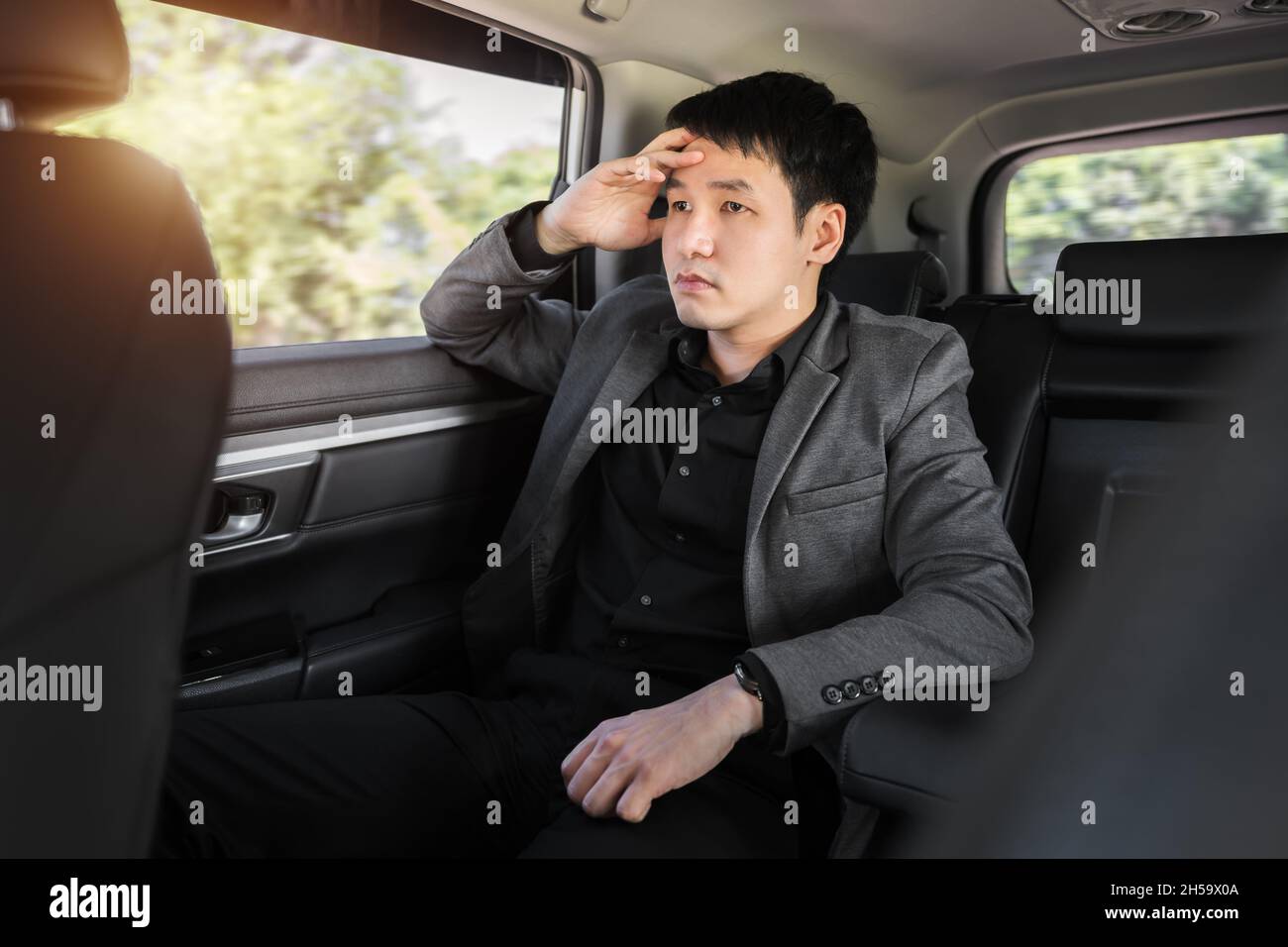 Gestresster junger Geschäftsmann, der auf dem Rücksitz des Autos sitzt Stockfoto