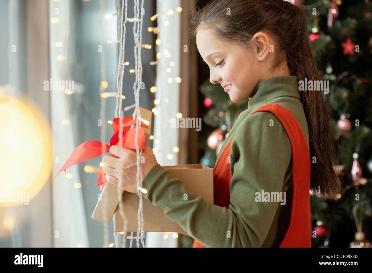 Lächelnd schönes Mädchen mit Pferdeschwanz stehen am Fenster mit Lichtern und Eröffnung Weihnachtsgeschenk Stockfoto