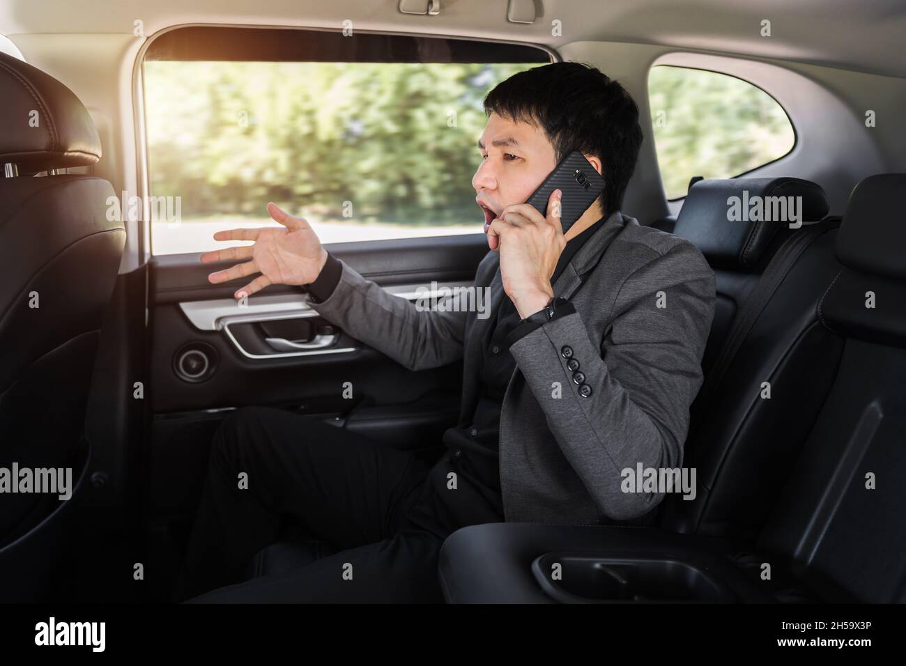 Gestresster junger Geschäftsmann, der auf dem Rücksitz des Autos sitzt und ein Problem mit einem Mobiltelefon spricht Stockfoto