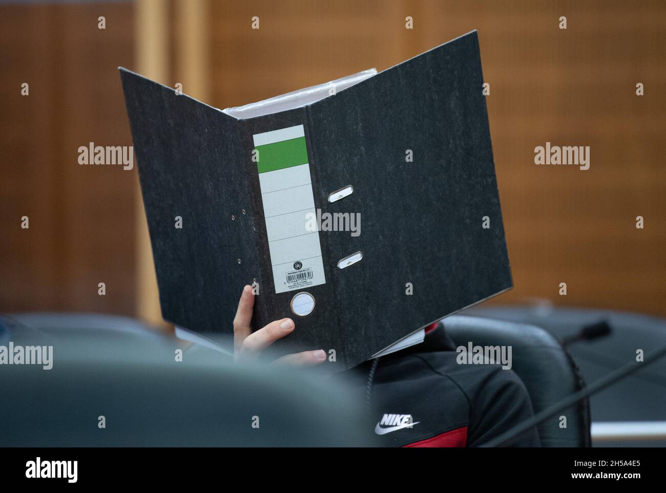 08. November 2021, Hessen, Frankfurt/Main: Der Angeklagte Iraker Taha Al-J. sitzt im Dock und versteckt sein Gesicht hinter einem Aktendeckel. Die Bundesanwaltschaft wirft ihm Völkermord, Verbrechen gegen die Menschlichkeit, Kriegsverbrechen, Menschenhandel und Mord vor. Als mutmaßliches Mitglied der Terrormiliz IS soll er eine yezidische Frau und ihre Tochter als Sklaven festgehalten und missbraucht haben. Dabei soll er den fünfjährigen in Falludscha, Irak, gefesselt haben, wo das Kind laut Anklageschrift vor Schmerzen verdurstet starb. Foto: Boris Roessler/dpa Stockfoto