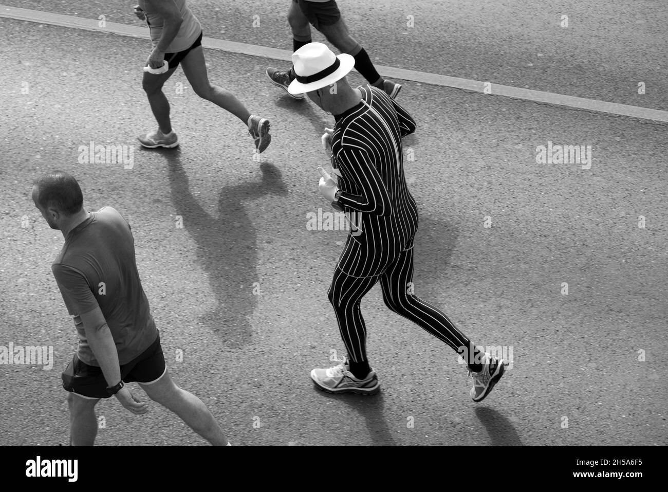 Mann in gestreiftem Trikot und Hut unter Marathonläufern. Schwarz und Weiß Stockfoto