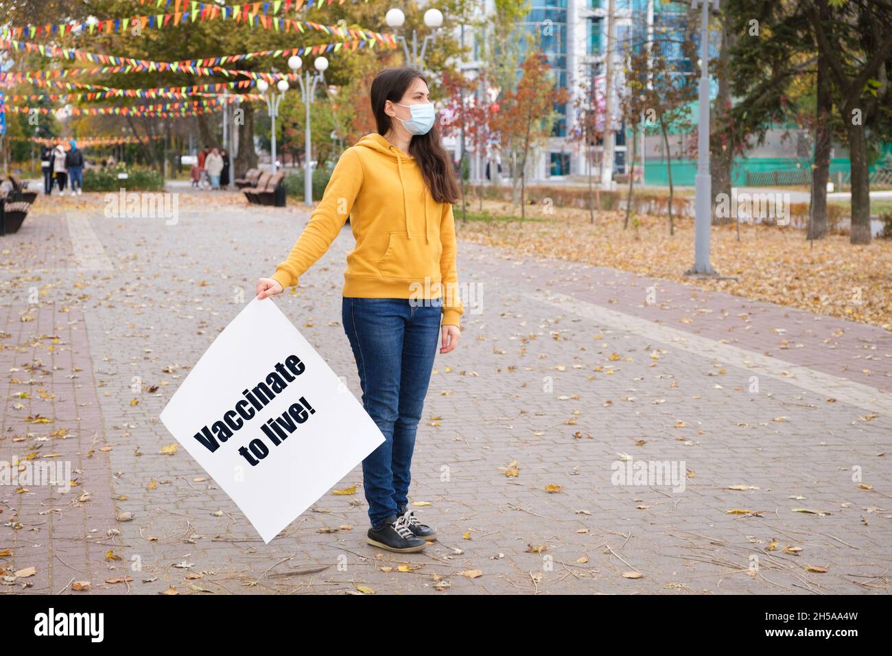 Eine Frau in einer medizinischen Maske hält ein Plakat, auf dem steht, impfen zu leben Stockfoto