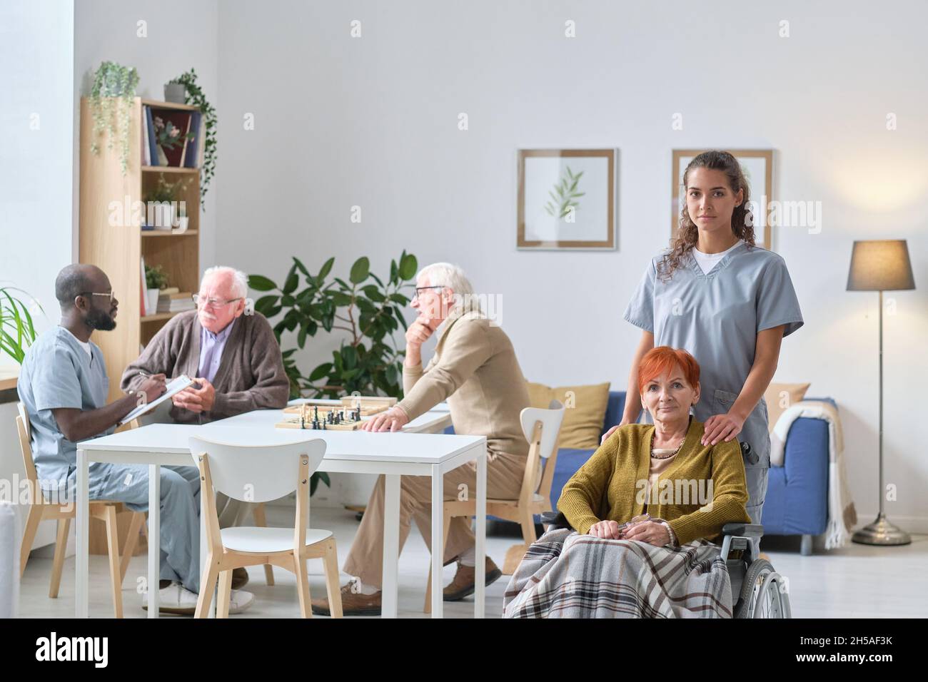 Porträt einer jungen Krankenschwester mit einer älteren Frau, die lächelt vor der Kamera während ihrer Arbeit im Pflegeheim kümmert sie sich um ältere Menschen Stockfoto